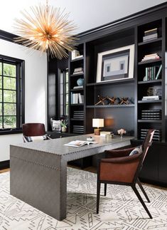 an office with black bookcases, leather chairs and a chandelier hanging from the ceiling