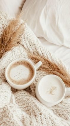 two cups of coffee are sitting on a blanket with wheat stalks in the foreground