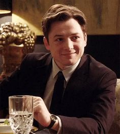 a man in a suit and tie sitting at a table with a glass of water