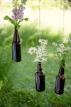 three brown bottles with flowers in them hanging from strings on the grass and some daisies