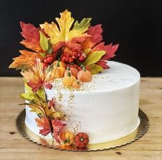 a white cake decorated with fall leaves and acorns on a wooden table top