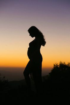 the silhouette of a pregnant woman at sunset