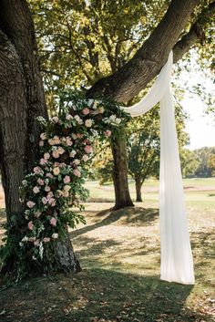 a wedding arch with flowers and greenery hanging from the side of a large tree