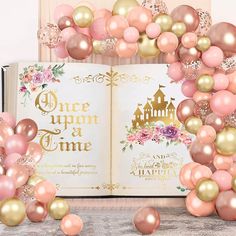 an open book surrounded by pink and gold balloons