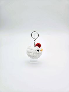 a white chicken keychain with a red hat on it's head is shown