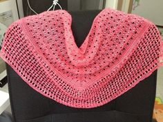 a pink crocheted shawl sitting on top of a black piece of furniture