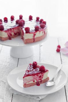 a piece of cheesecake with raspberry topping on a white cake plate next to the rest of the cake