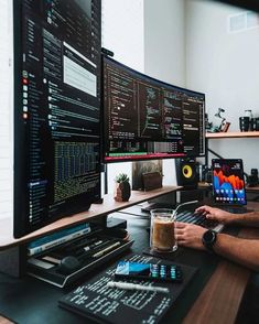 a man sitting at a desk with two computer monitors and a drink in front of him