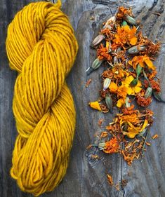 a skein of yellow yarn next to dried flowers on a wooden surface with wood planks