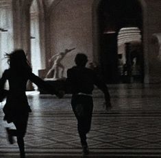 two people are running in the middle of a room with marble flooring and walls