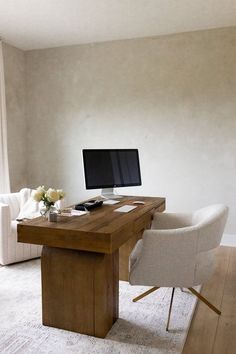 a desk with a computer on it in front of a couch and chair next to a window