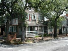 an old wooden house sitting on the side of a road next to trees and bushes