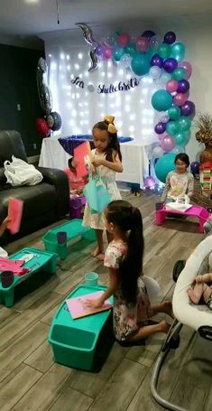 several children are sitting on the floor in front of balloons and other decorations, while one child is holding a toy