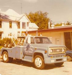 an old blue tow truck parked in front of a house with a crane on it's back