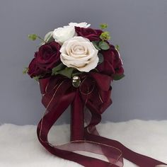 a bridal bouquet with white and red roses on a burgundy ribbon tied around it