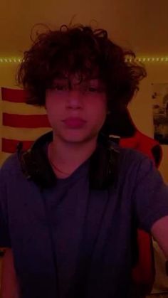 a young man with curly hair is taking a selfie in front of an american flag