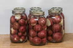 three jars filled with red potatoes sitting on top of a wooden table