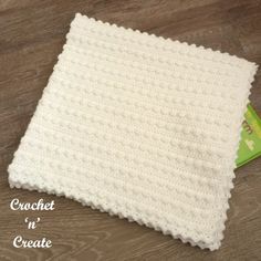 a crocheted blanket sitting on top of a wooden floor next to a book