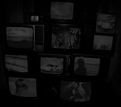 black and white photograph of televisions in dark room