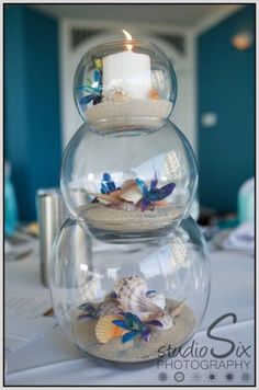 three glass vases filled with sand and seashells on top of a table