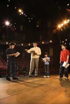 several people standing on a stage with microphones in their hands and one person holding papers