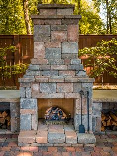 an outdoor fireplace is shown in the middle of a patio with brick pavers and firewood stacked on each side