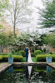 a bride and groom standing on the edge of a pond in front of some bushes