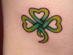 a shamrock tattoo with two hearts on the side of her leg and an intertwined green ribbon