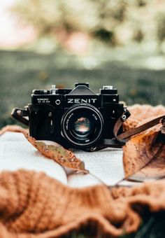 an old camera sitting on top of a blanket next to a book and some leaves