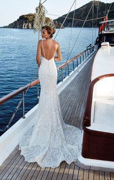 a woman standing on the deck of a boat looking out at the water while wearing a wedding dress