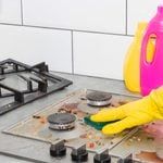 a person in yellow gloves cleaning a stove top with a pink and yellow sprayer