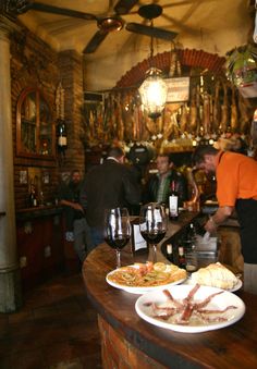 two plates of food on a bar with people standing in the background and hanging from the ceiling