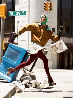 a woman in red tights and green head scarf is walking past a trash can