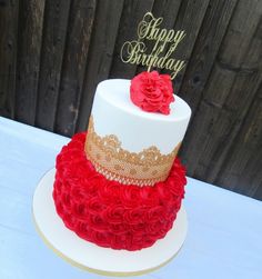 a red and white birthday cake with gold trimmings on a table next to a wooden fence