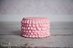 a pink cupcake with ruffles sitting on top of a wooden table next to a wall