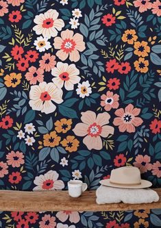 a wall with flowers on it next to a hat and coffee cup in front of the wall