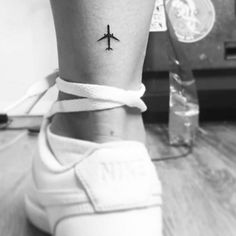 a small tattoo on the ankle of a woman with an airplane in the sky behind her