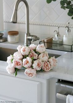 a bunch of pink flowers sitting on top of a kitchen counter next to a sink