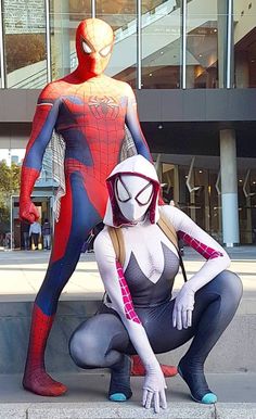 two people dressed up as spider - man and the amazing spider woman in front of a building