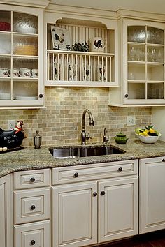 a kitchen with white cabinets and granite counter tops, along with an open shelf above the sink