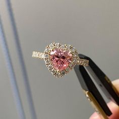 a pink and white diamond ring being held by someone's hand with two black tongs