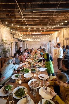 a group of people sitting at a long table eating food and drinking wine in a restaurant