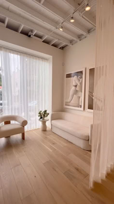 a living room filled with furniture and a window covered in white sheer curtaining next to a wooden floor