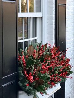 a window sill with red berries and greenery in front of a white brick building