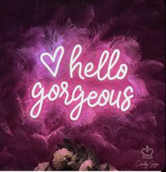 a neon sign that says hello gorgeous with pink feathers and flowers in front of it