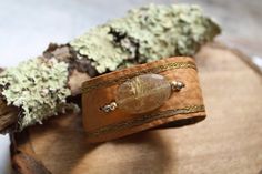 a brown leather bracelet with a stone bead on it and moss growing in the background