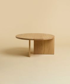 a round wooden table sitting on top of a white floor next to a beige wall