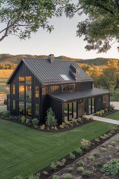 a large black house sitting in the middle of a lush green field with lots of trees