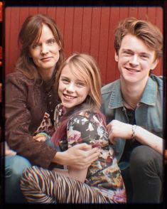 three people sitting next to each other on a couch with a red wall behind them