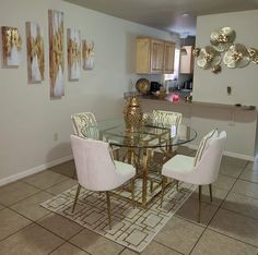 a dining room table with white chairs and gold accents on the wall above it is an area rug